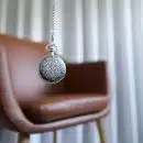 silver round pendant on brown wooden chair