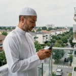 Homme musulman consultant les heures de prière sur smartphone depuis un balcon à Bondy